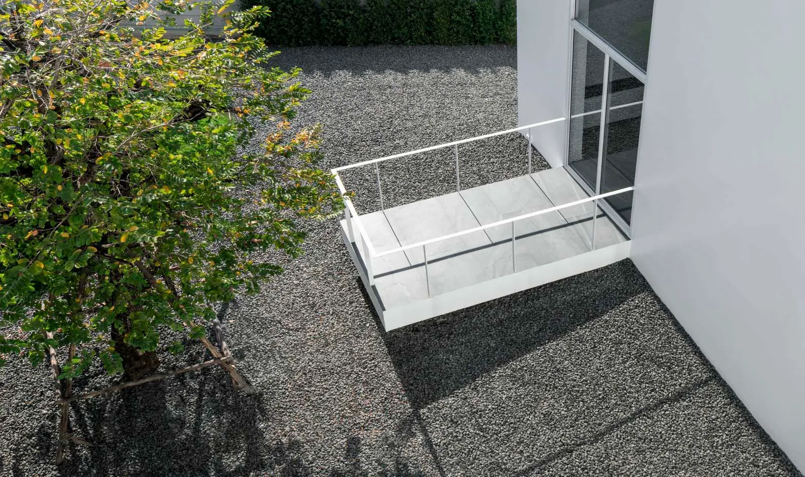 Modern exterior space featuring a concrete terrace with glass railings and gravel path.