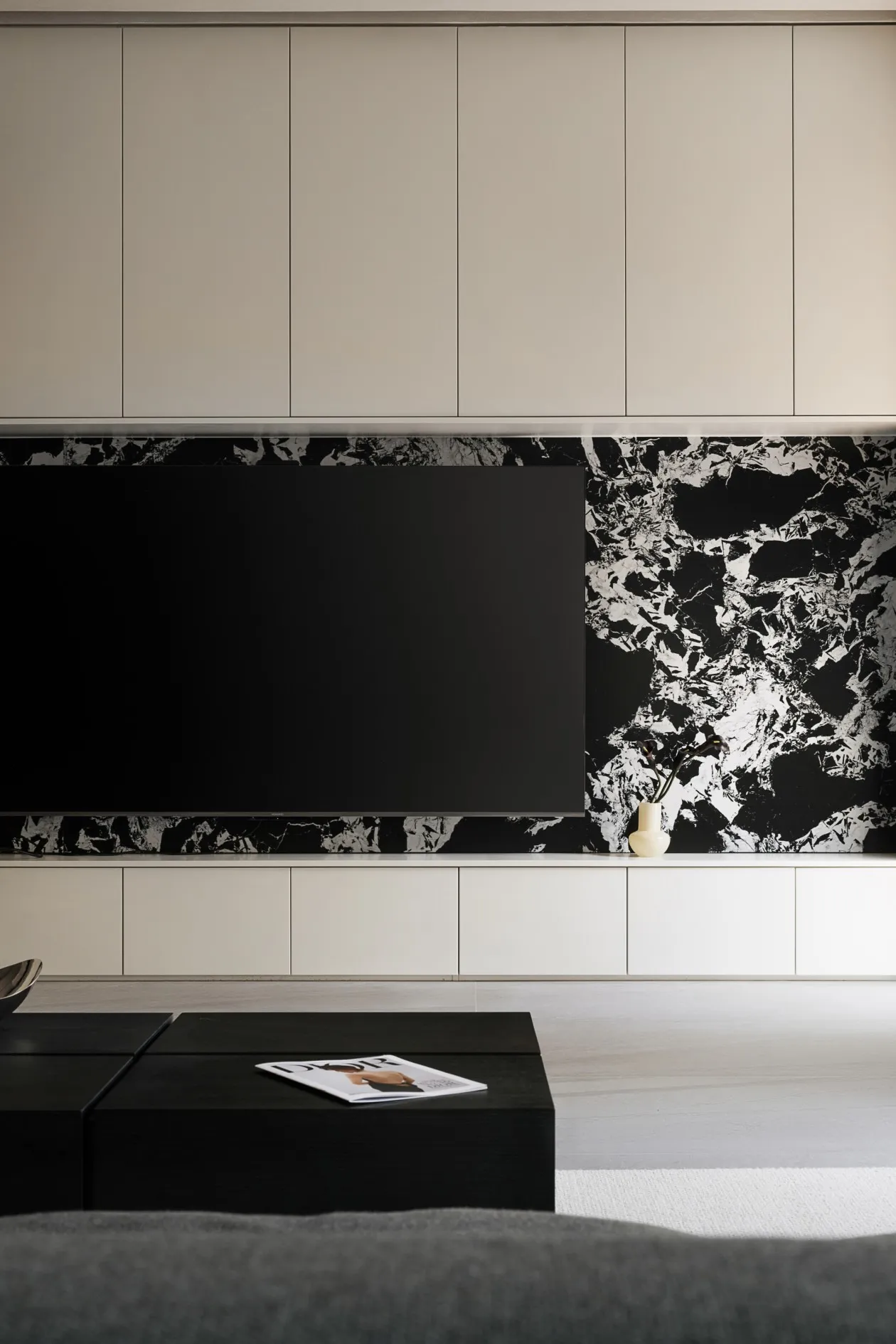 A modern minimalist living room featuring a large black flat-screen TV mounted on a black and white marble wall with a white 