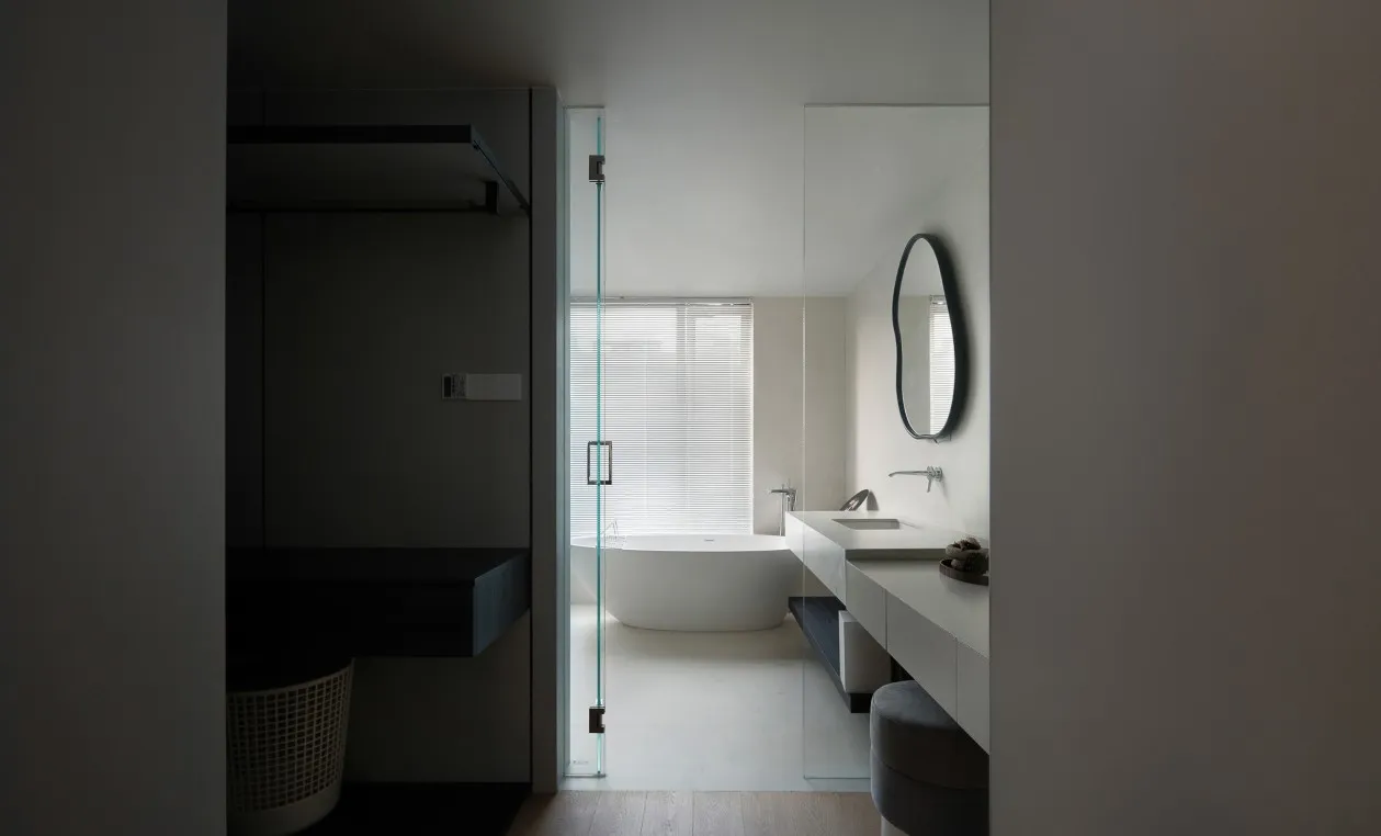 Modern minimalist bathroom with a freestanding glass shower enclosure, white porcelain sink, and a large window with white bl
