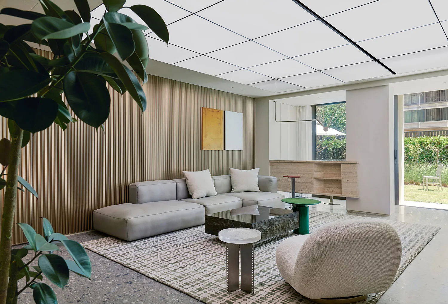 A minimalist living room with concrete and glass elements, featuring a modern sofa, coffee table, and a green stool.
