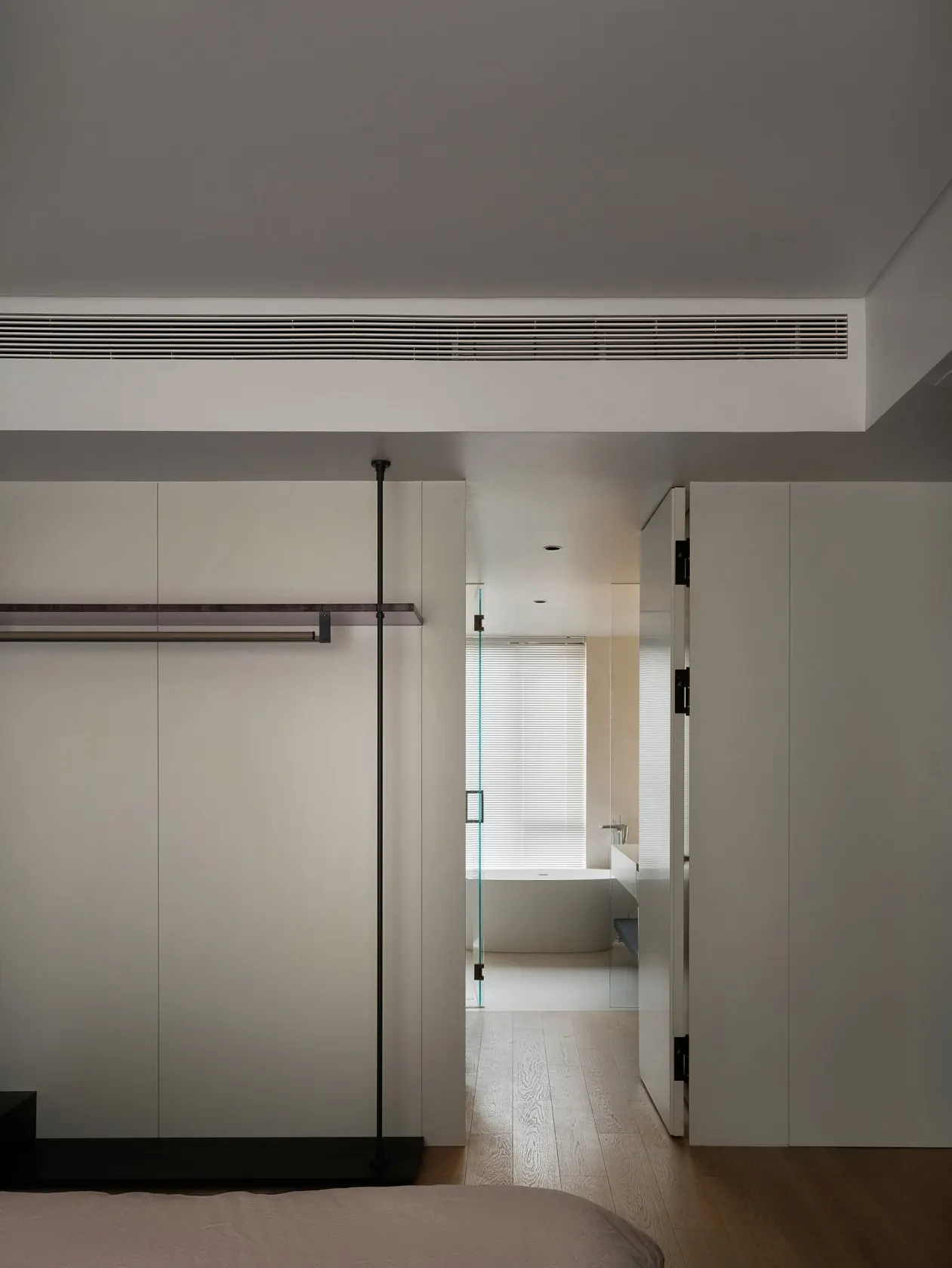 A minimalist bedroom with white walls, a wood floor, and simple furniture