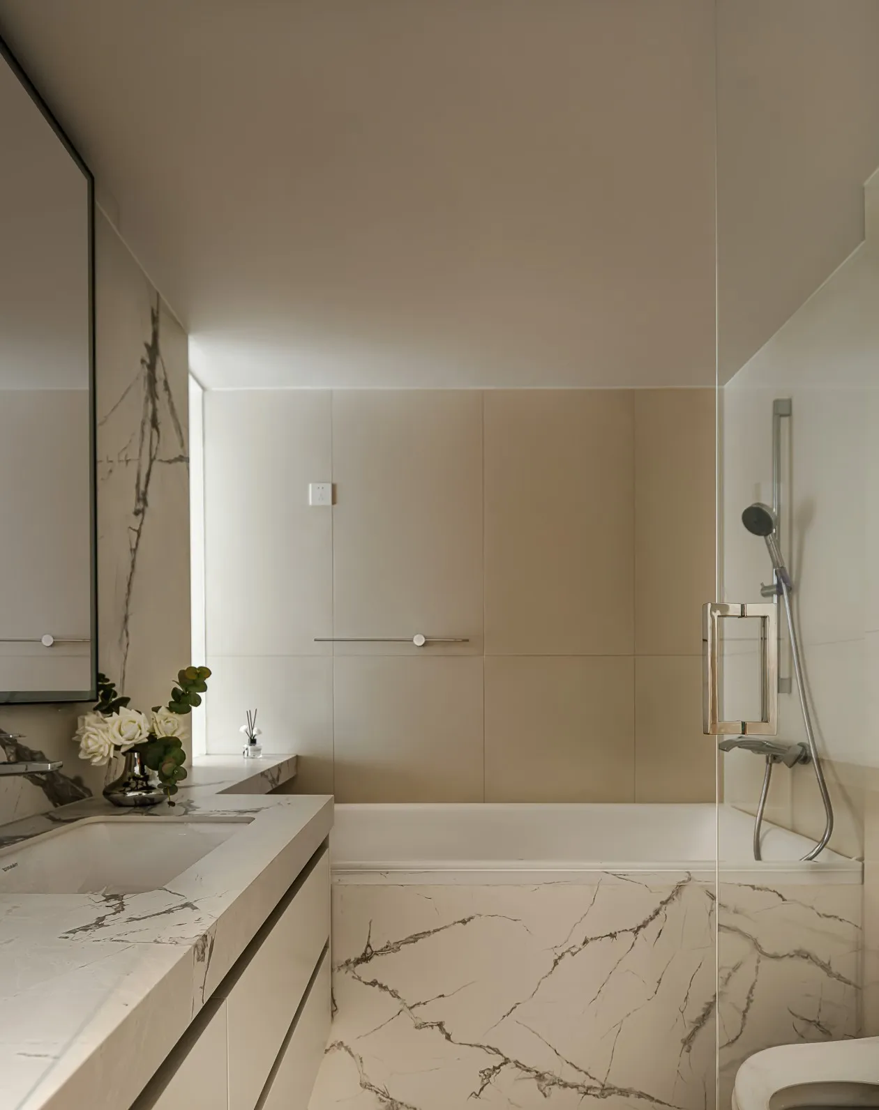 Modern minimalist bathroom with white marble vanity and tub, glass shower enclosure, and beige tiled walls.