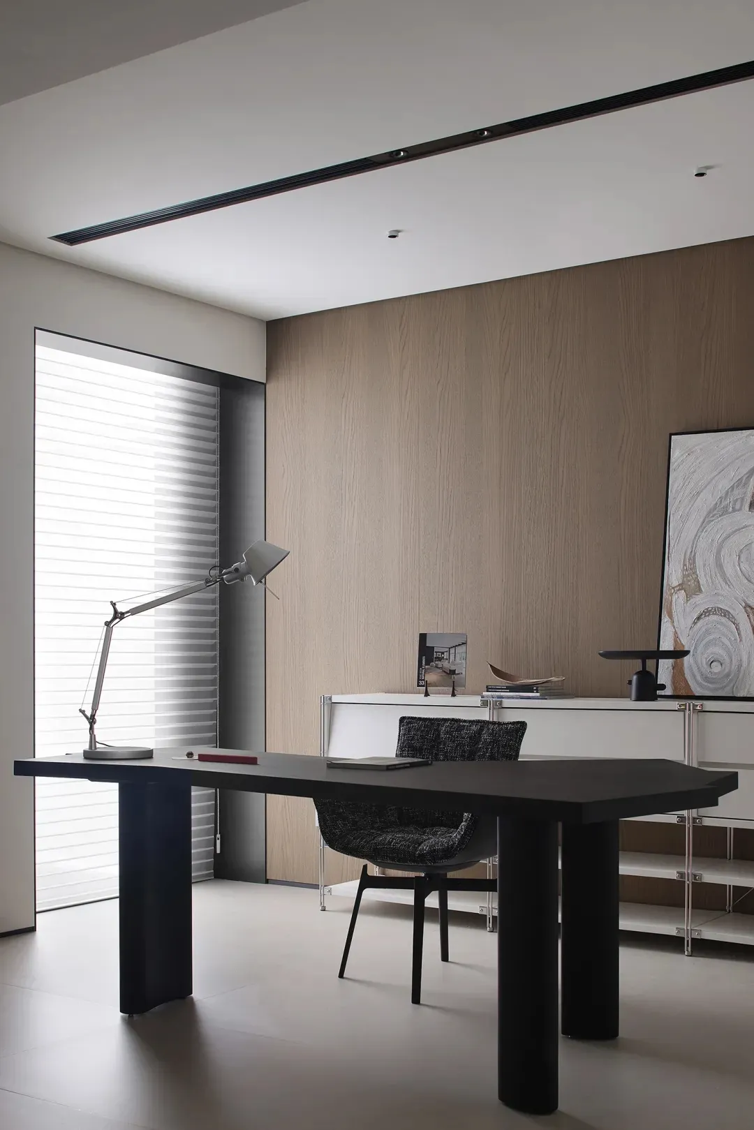 A minimalist office workspace with a wooden desk and chair, featuring a desk lamp and various items on the desk in a well-lit