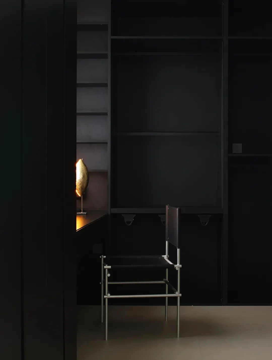 A minimalist wardrobe with black metal frame and shelves, illuminated by a golden lamp.