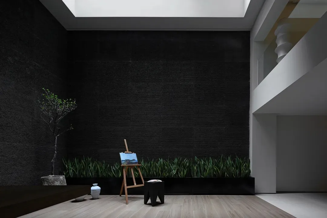 Modern living room featuring a dark textured wall, a small tree, and a painting on an easel.