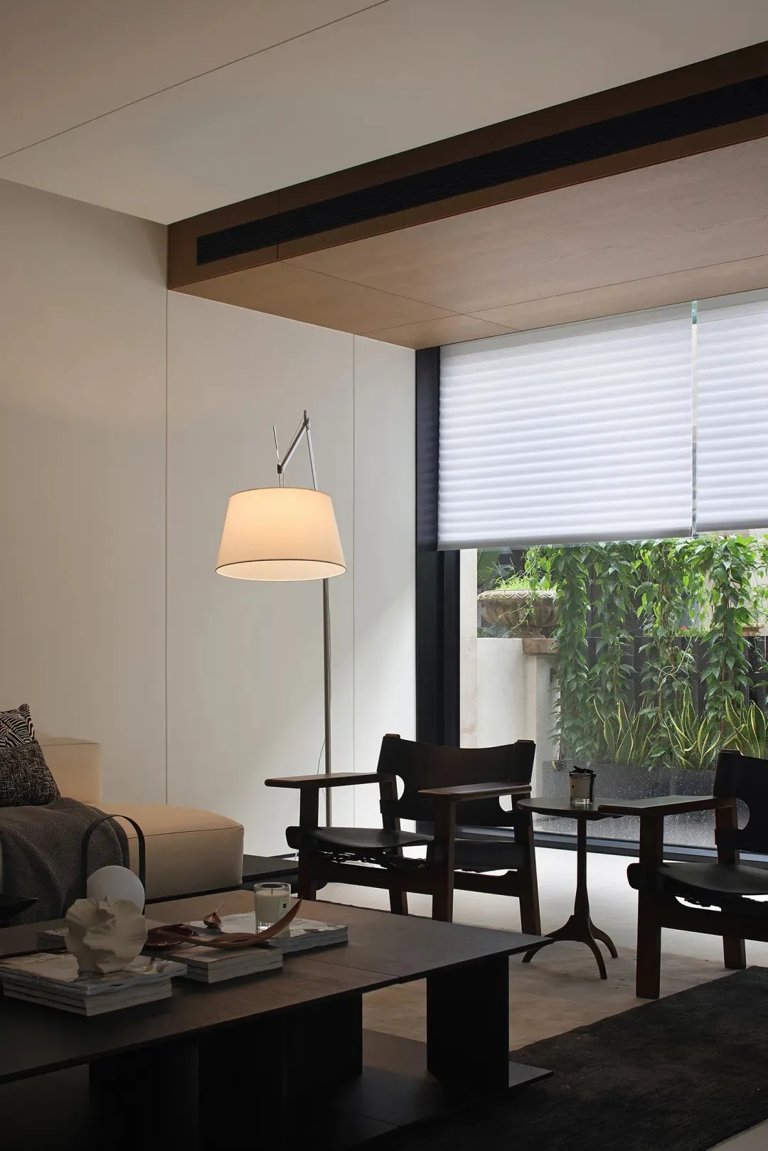 A modern indoor living room with wooden furniture and a large window, illuminated by a white floor lamp.
