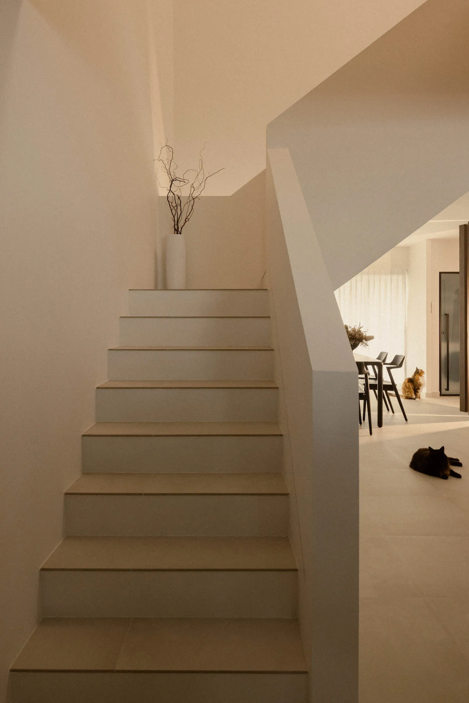 A modern, minimalist staircase with white concrete treads and modern railings, featuring a vase with dried branches on top of