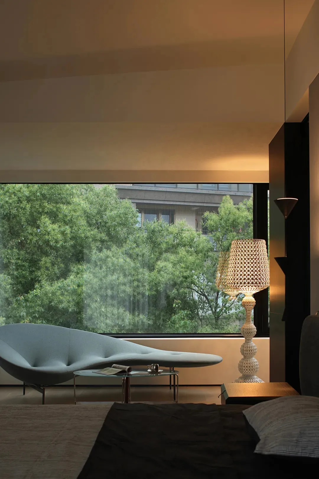A modern bedroom featuring a glass window with a view of green trees outside.