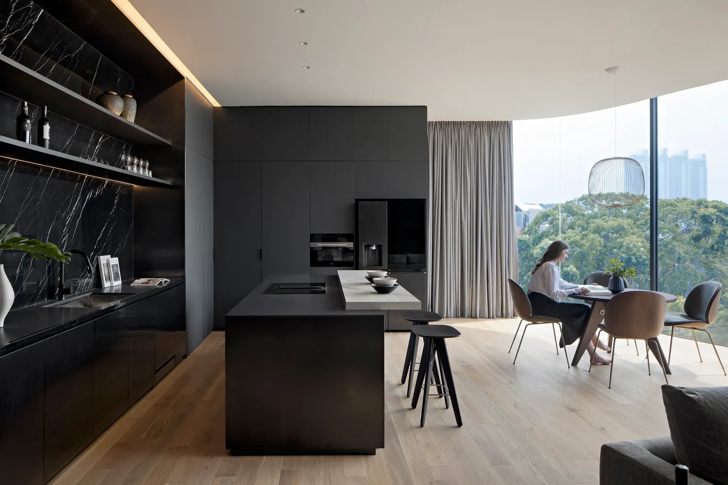 A modern kitchen and dining room featuring black marble countertops, black steel cabinets, and light wood flooring.
