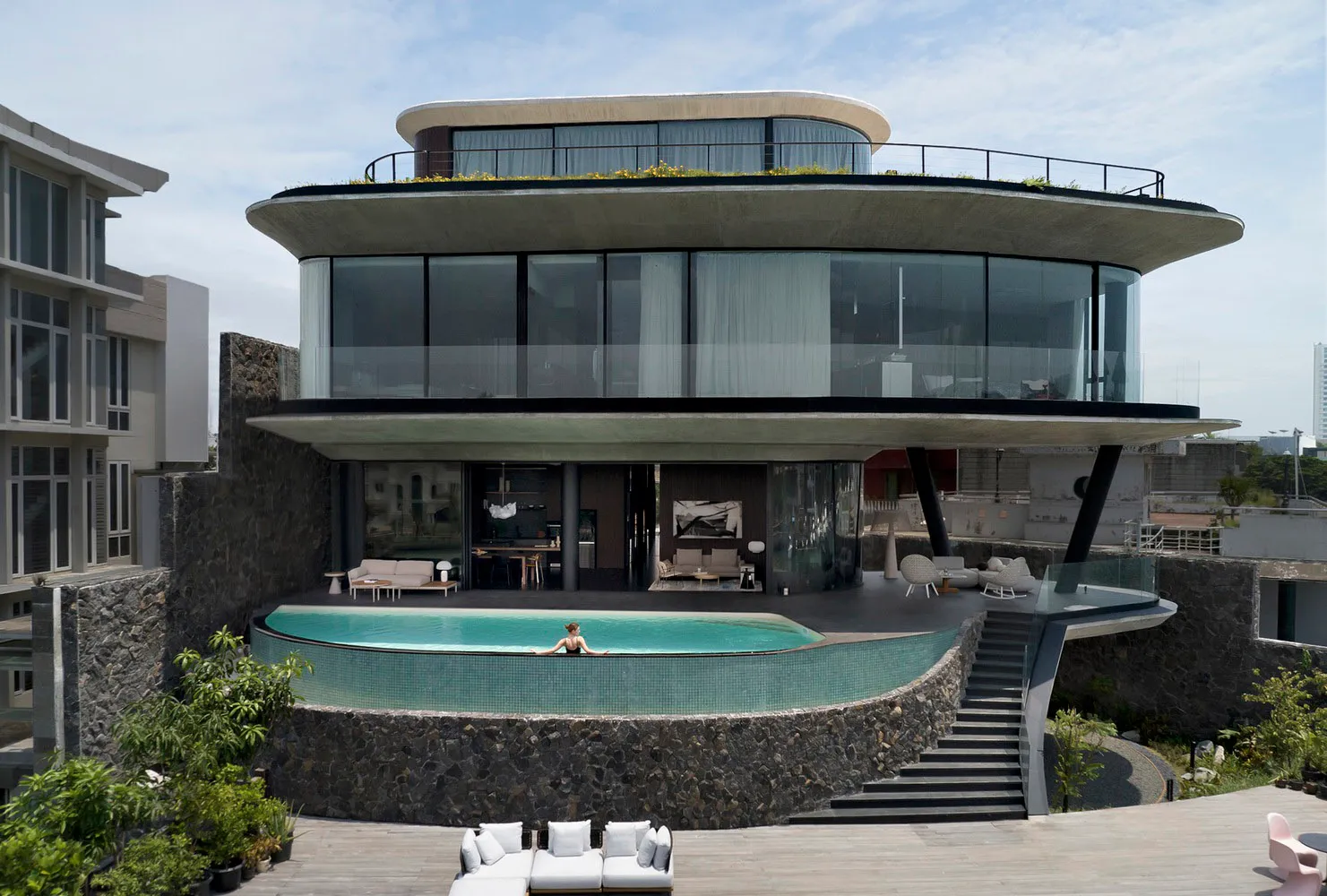 A modern house featuring a concrete exterior and glass elements with a person relaxing in the pool.