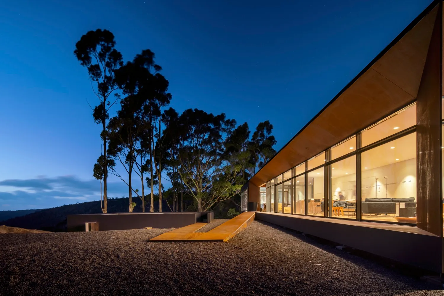 A modern house with metal cladding at dusk, featuring large windows and a minimalist design.