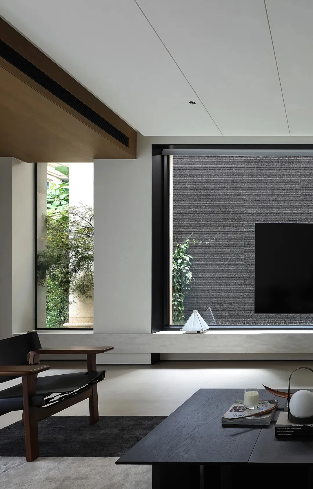 Modern living room with wooden armchair, coffee table, and concrete floor, featuring a television and plants.