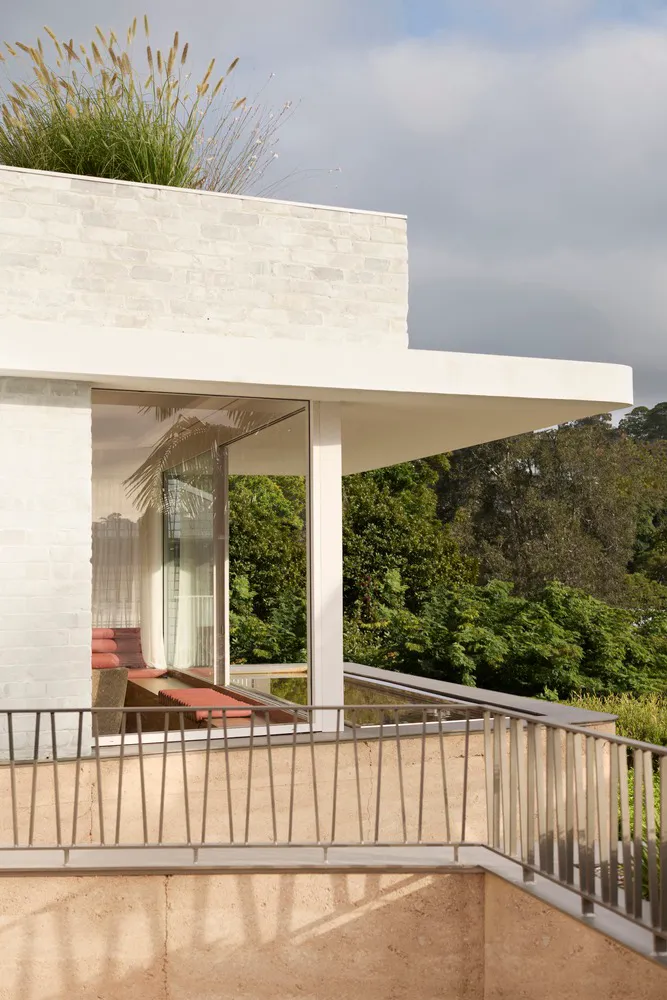 A modern residential building with a concrete exterior and glass windows, set against a backdrop of greenery.