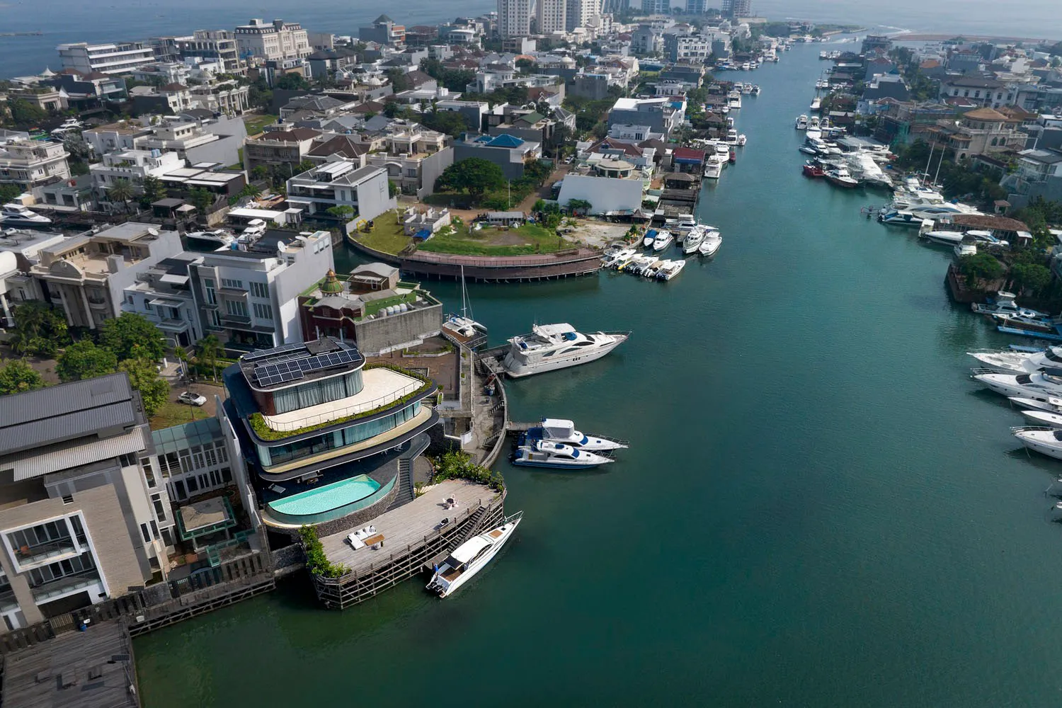 Aerial view of a waterfront development featuring concrete, glass, and timber structures with a pool and marina.