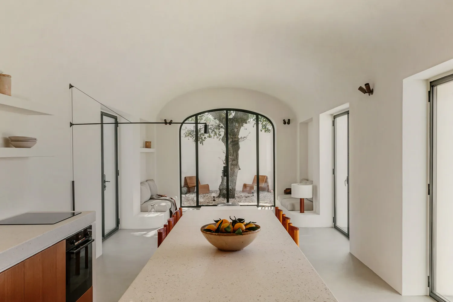 A minimalist residential dining room featuring concrete elements and a bowl of oranges on the table.