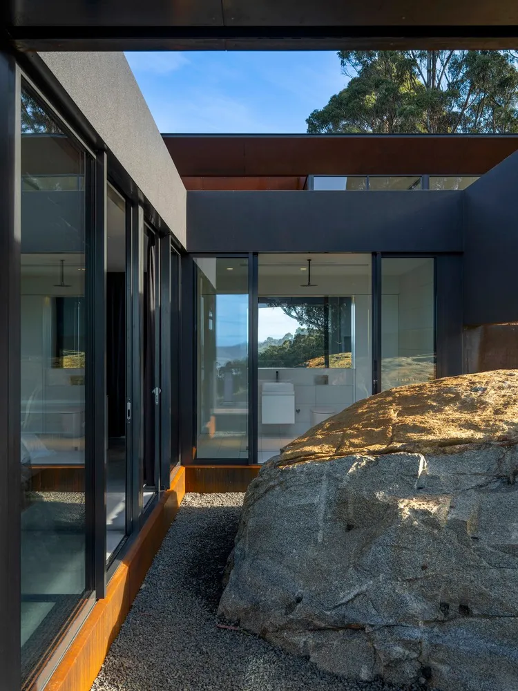 Modern house entry with glass cladding, featuring large glass doors and a stone rock.