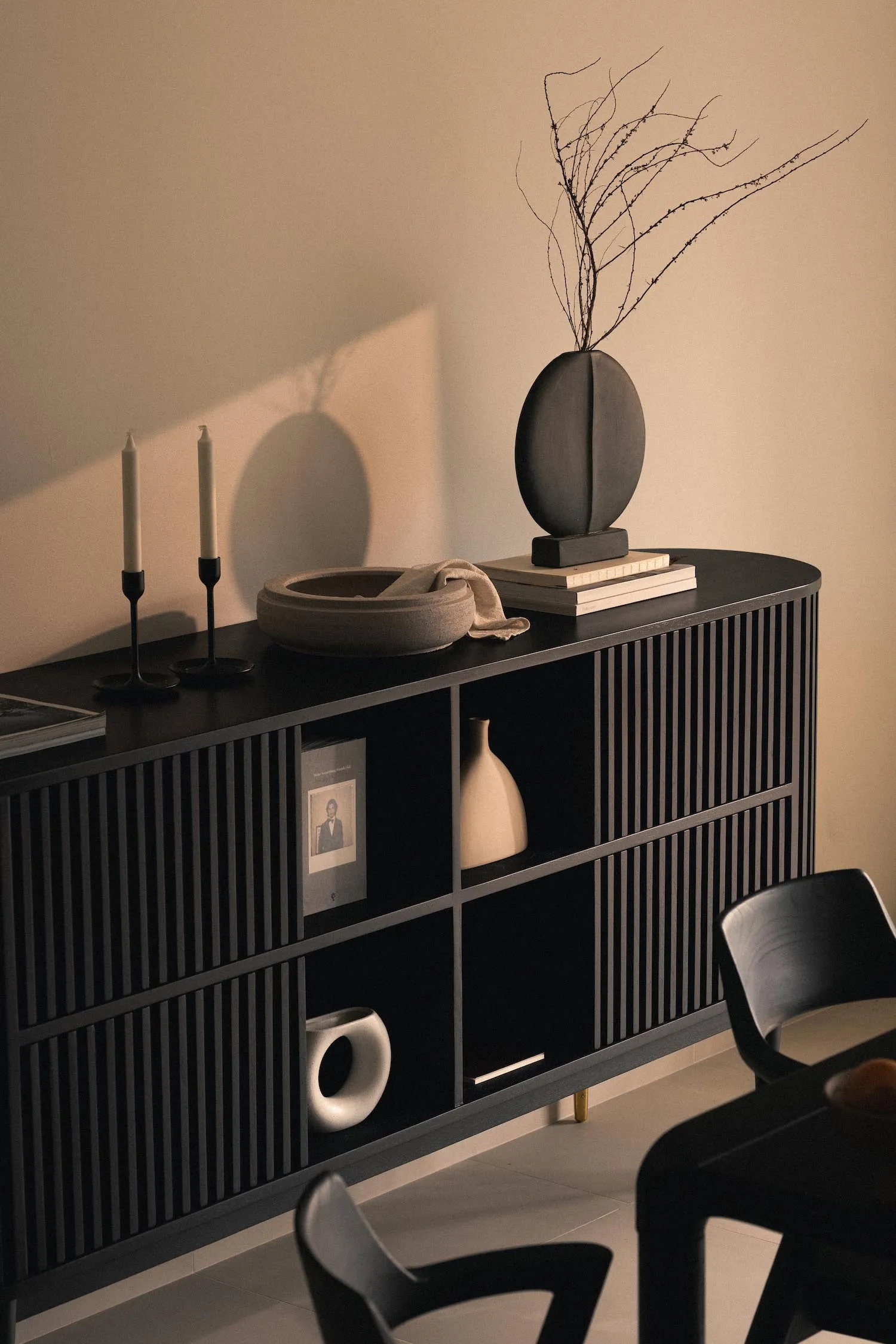 A modern sideboard made of black wood with geometric patterns, featuring decorative items such as a vase, candles, and books.