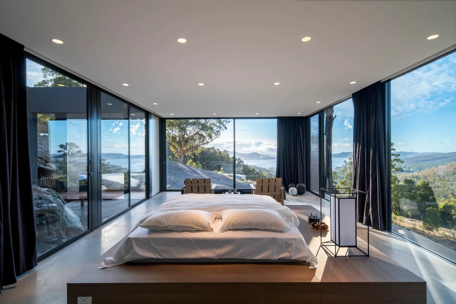 Modern bedroom featuring wood flooring, glass walls, and a view of the landscape.