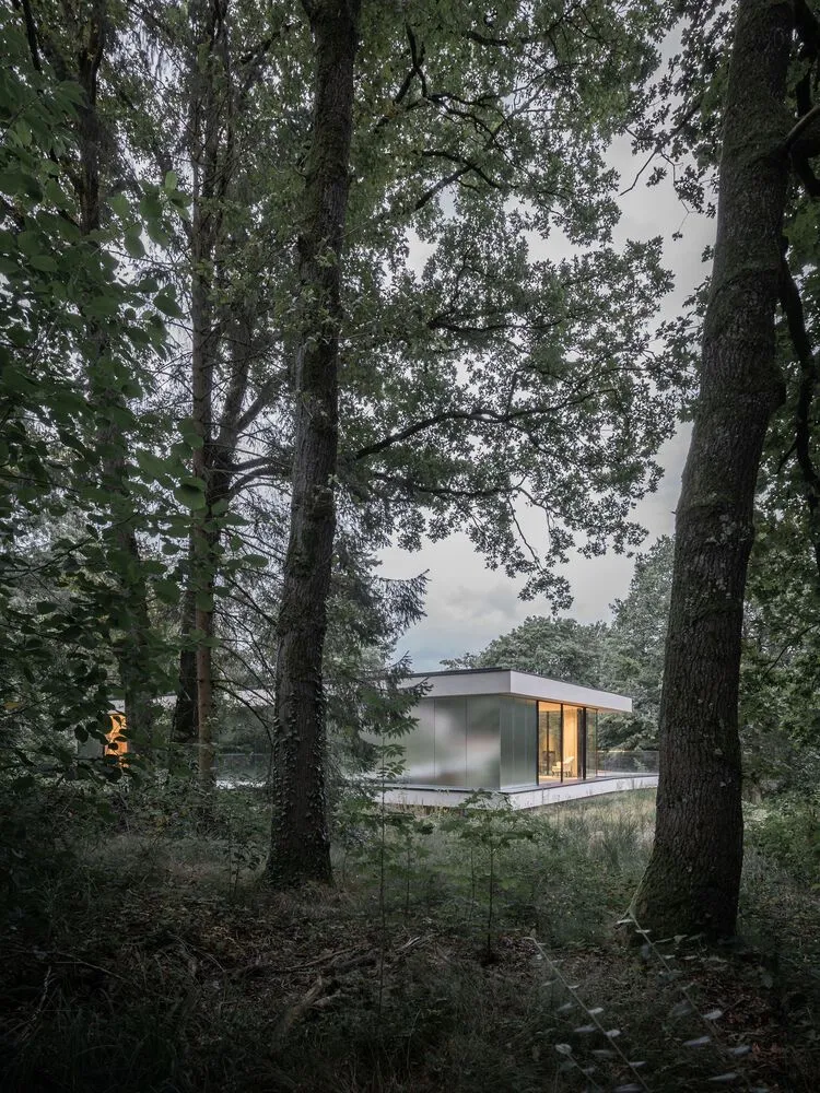 A minimalist house with glass walls nestled in a forested area.