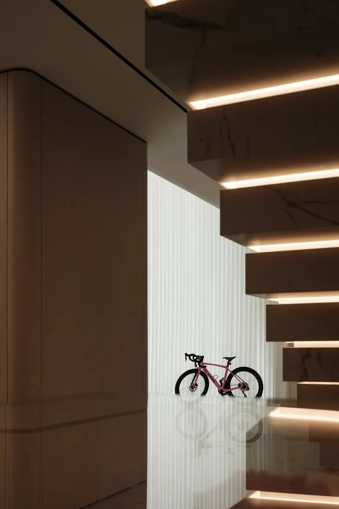 A minimalist interior design featuring a bike displayed below a modern marble staircase.