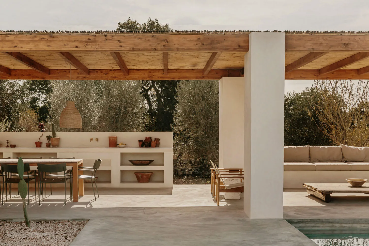 Outdoor living area with minimalist design, concrete floor and walls, wooden accents, and greenery in the background.