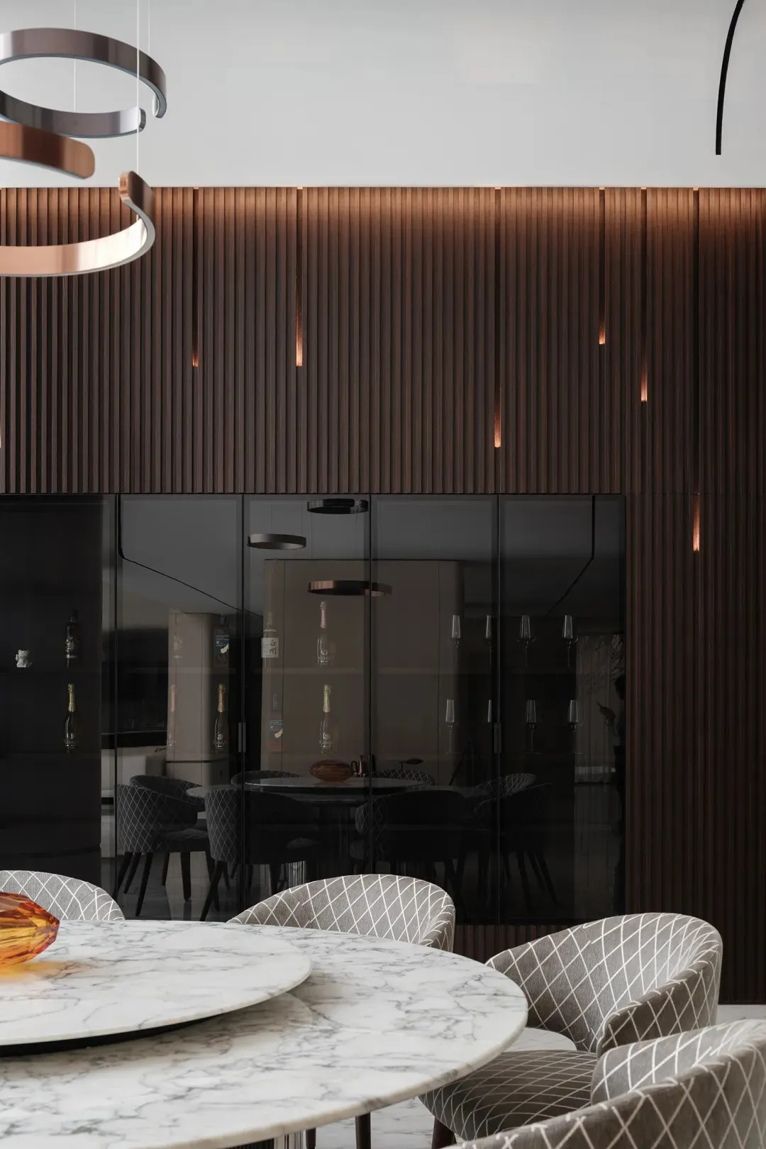 Modern dining room featuring a round marble table surrounded by upholstered chairs, with a wall of vertical wood panels and b