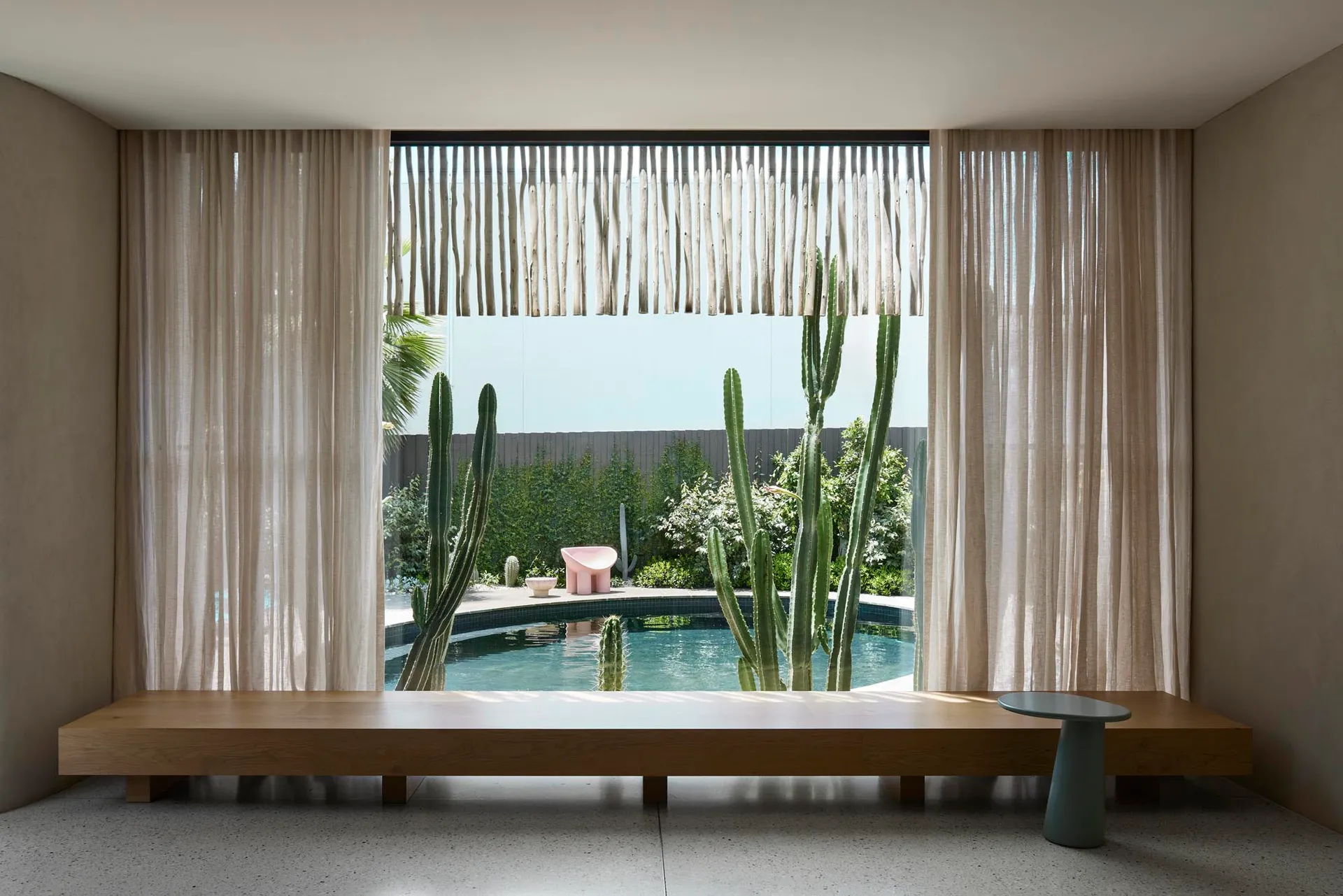 Minimalist residential interior with a large window overlooking a pool and cactus garden.