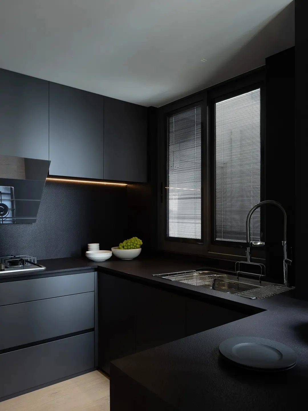 A modern, minimalist black kitchen with granite countertops, featuring a sink, stove, and minimalist design elements.