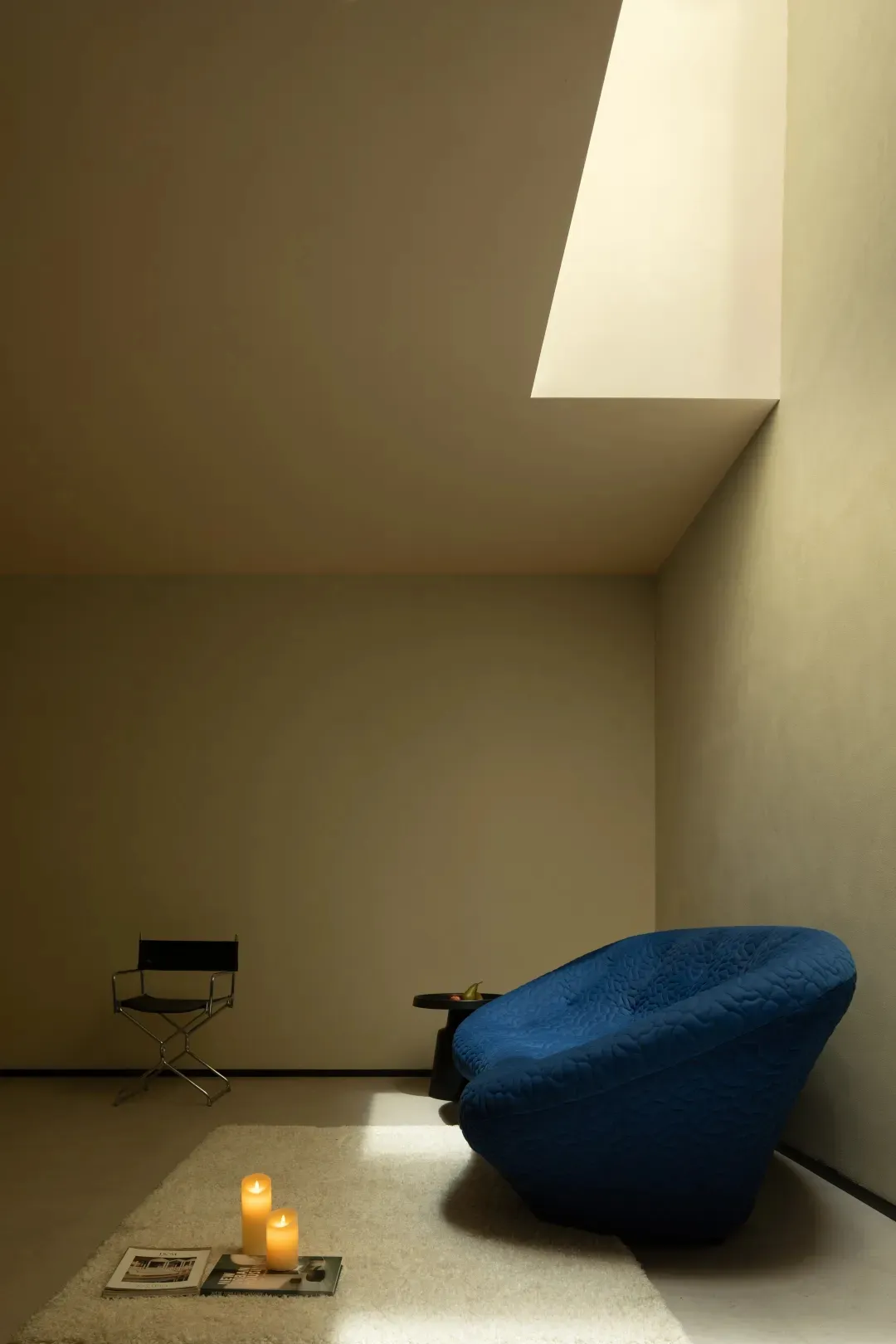 A minimalist living space featuring a modern blue sofa on a white rug, with candles and magazines.