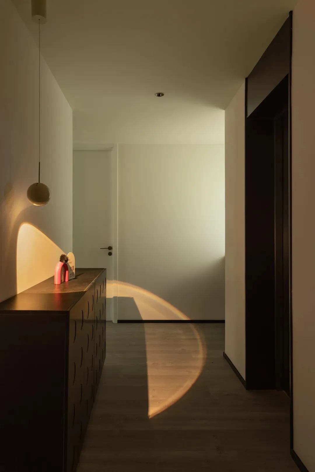 Modern corridor with concrete walls, wooden floors, and a hanging lamp casting light onto the floor.