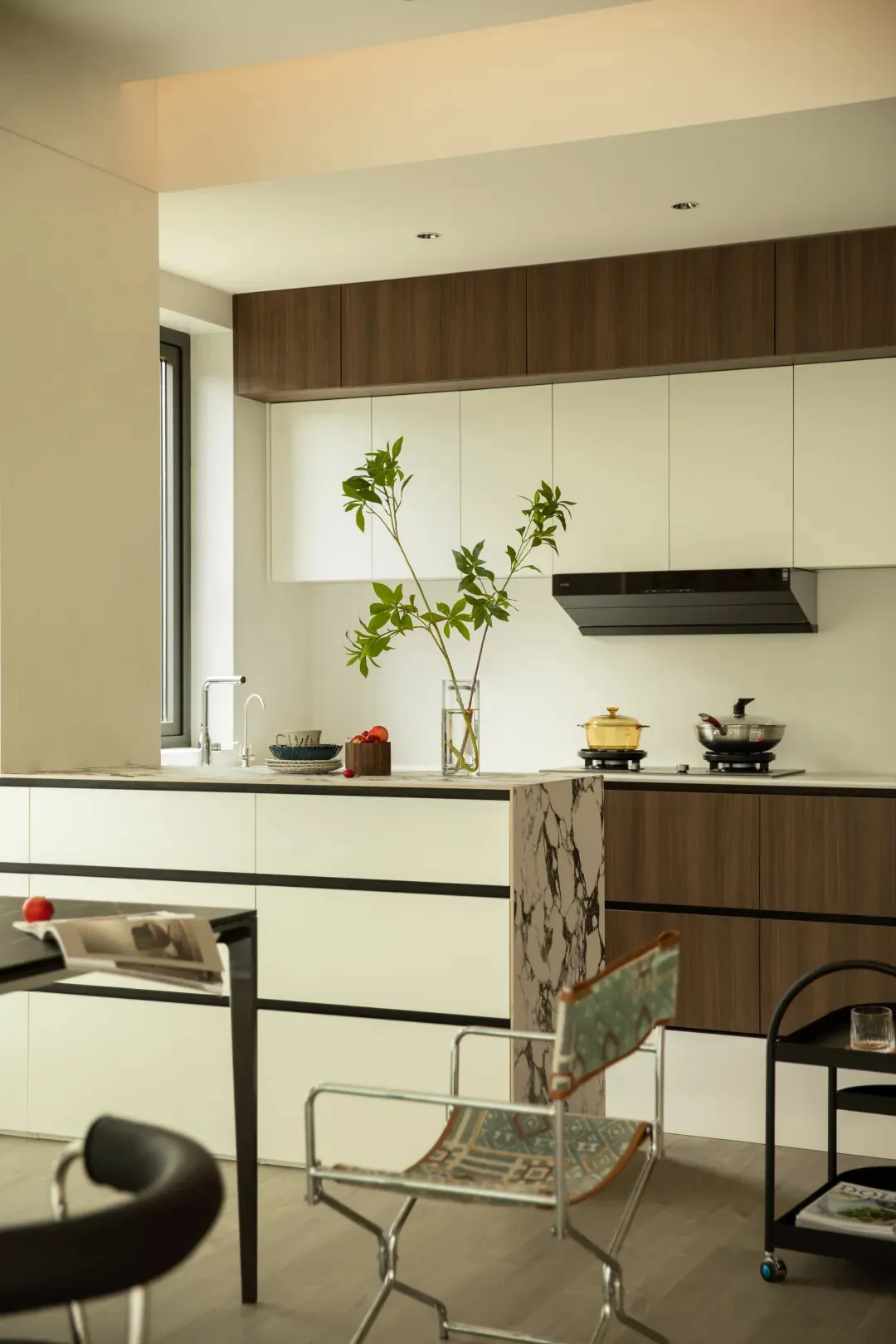 A modern kitchen with white marble countertops, wooden cabinets, and a black marble column.