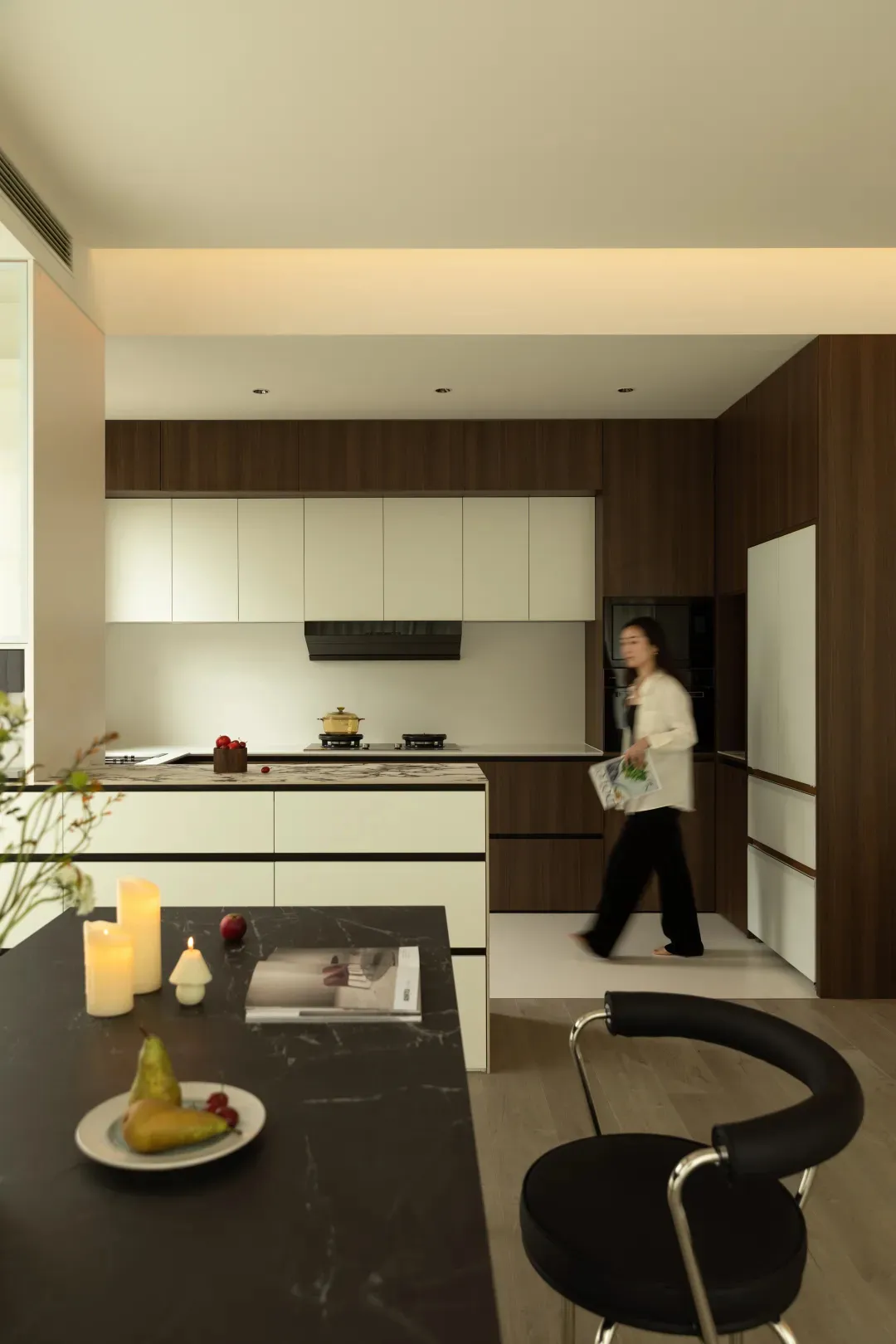 A modern kitchen featuring sleek wood cabinets and a marble countertop, with a woman walking past.
