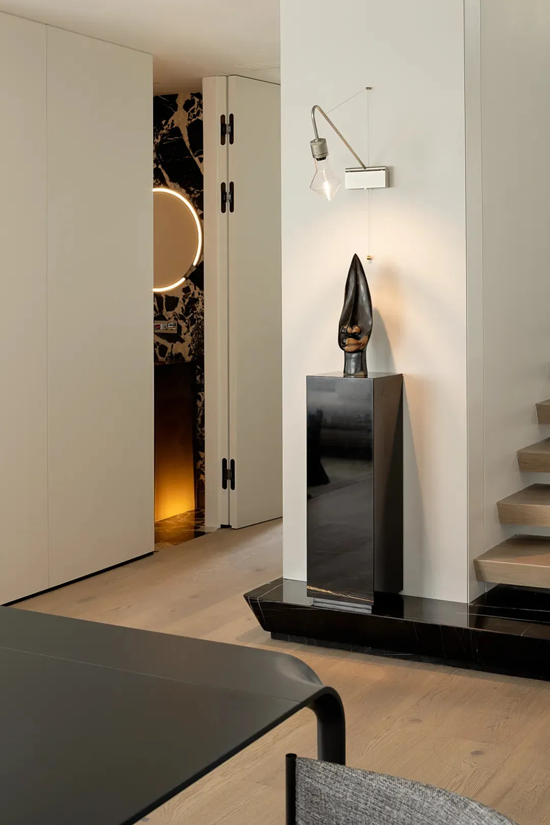 Modern hallway featuring concrete walls and floors, with a hanging light fixture and a sculptural artwork on a pedestal.