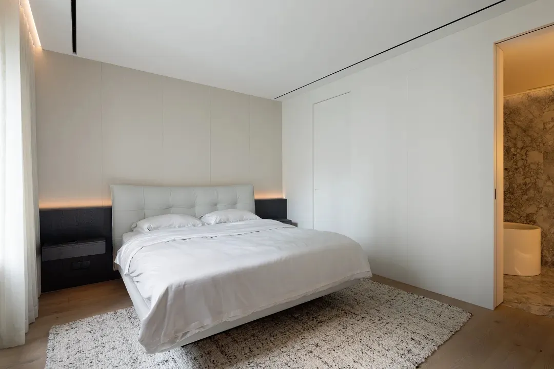 Minimalist bedroom with a white leather platform bed, neutral-toned walls, and a textured rug.