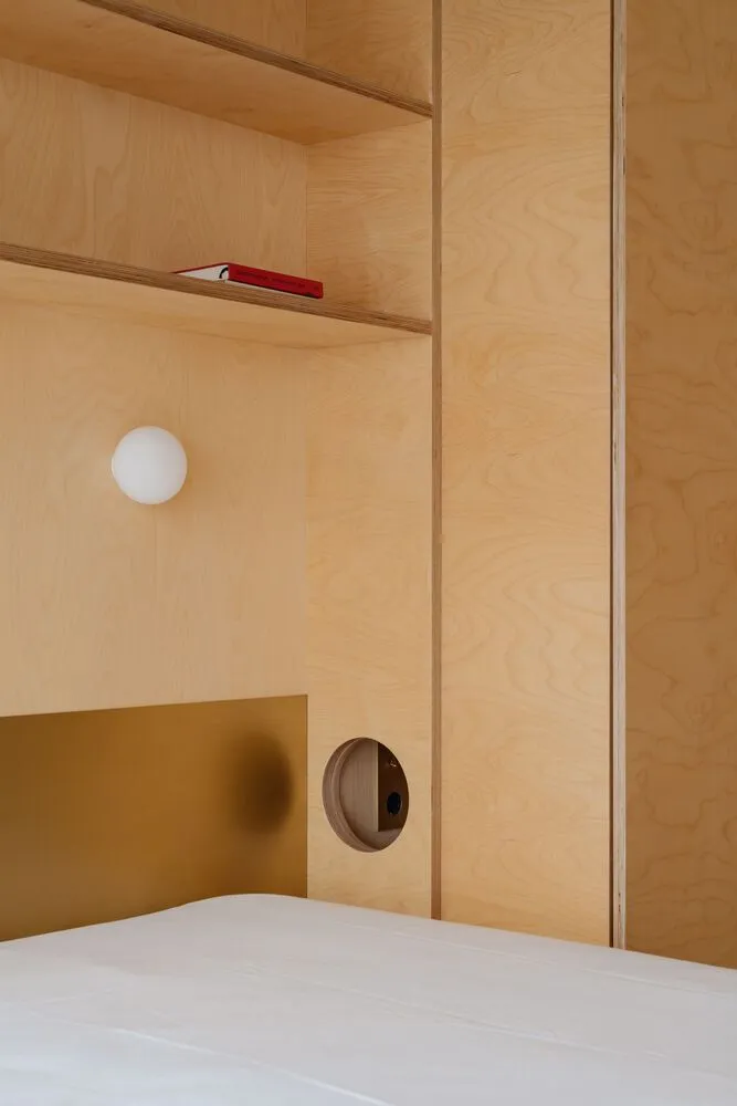 A minimalist bedroom featuring wooden shelves and a white bed.