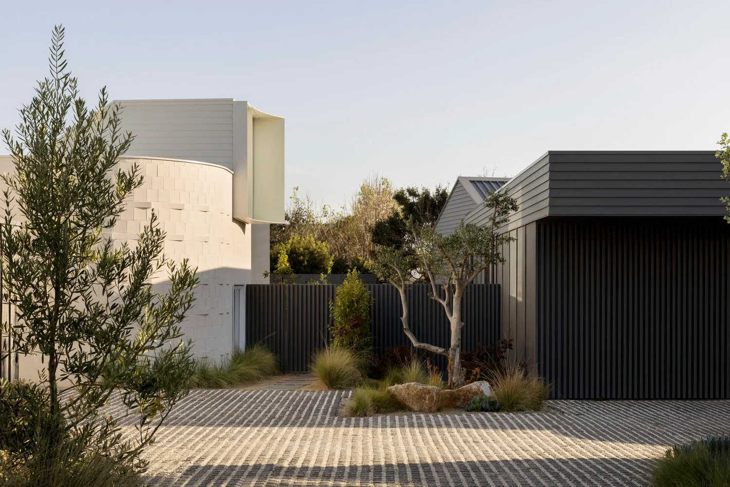 Modern minimalist house featuring concrete and metal exteriors, with landscaping and a patterned driveway.