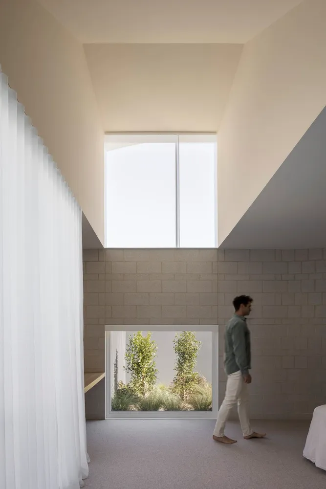 A minimalist house with concrete walls and a high ceiling, featuring a large window looking out to a green space.