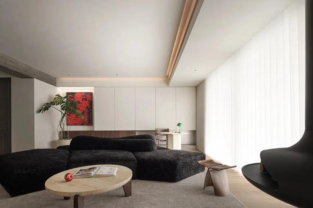 A minimalist living room with a black upholstered sofa, a wooden coffee table, white cabinetry, and glass panel drapes.