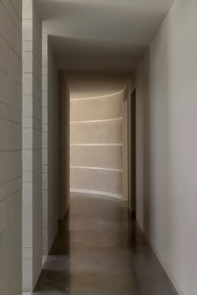 A modern concrete corridor with curved walls leading to a light source at the end.