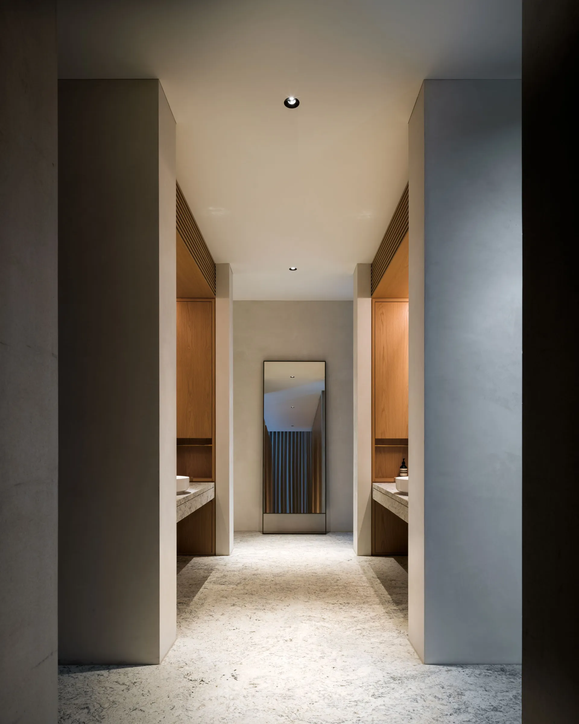 A minimalist bathroom with concrete flooring, wooden cabinets, and a large mirror.