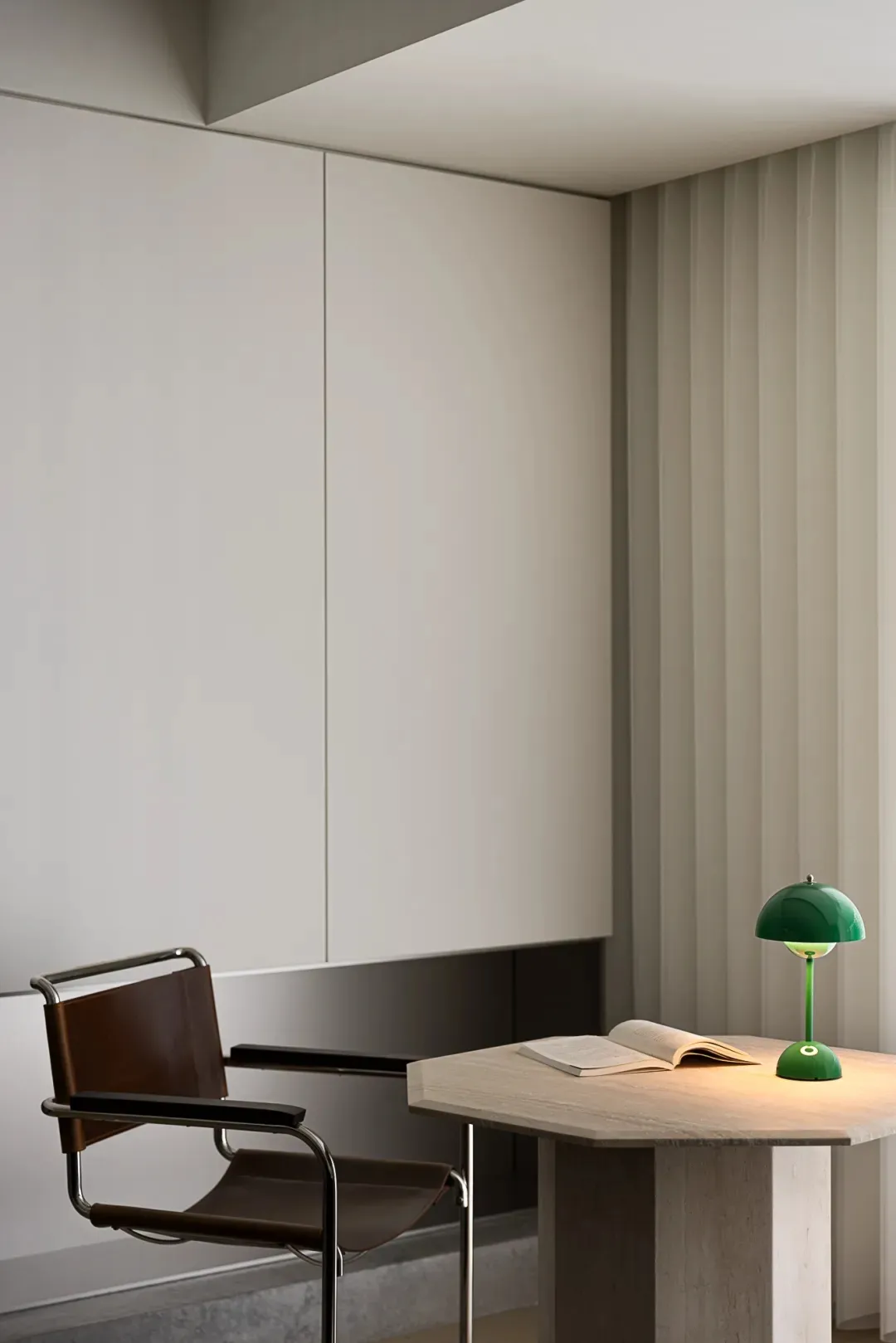 A minimalist office space featuring a concrete table, leather chair, and green table lamp.
