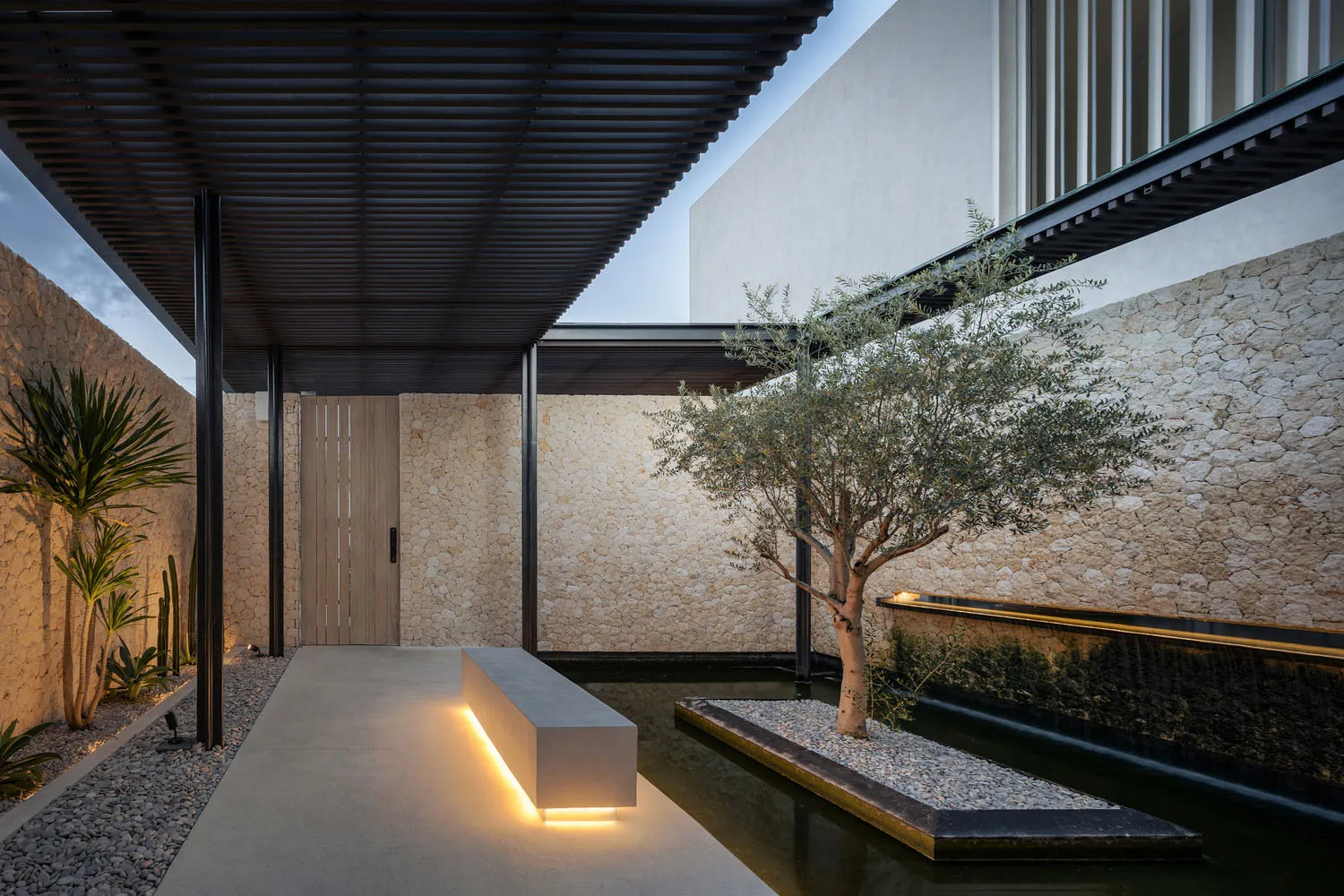 A modern residential entrance featuring a concrete ground with an embedded light source and a tranquil water feature with an