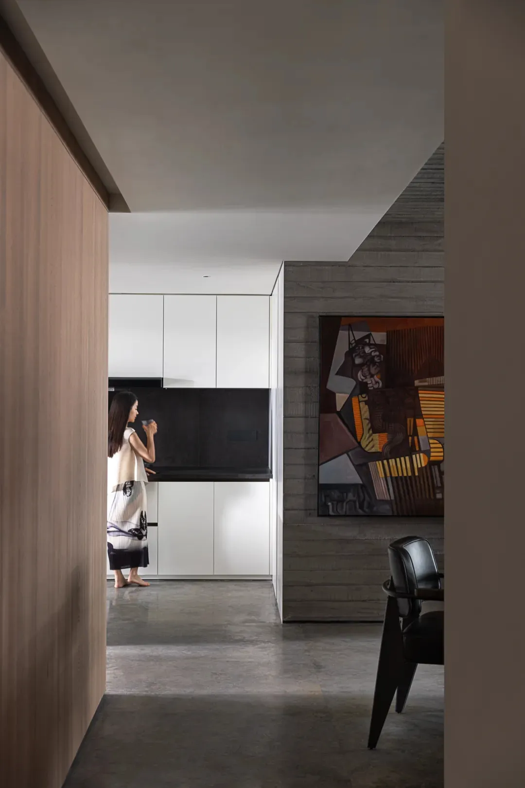 A modern minimalist kitchen with concrete walls, featuring sleek white cabinets and black countertops.
