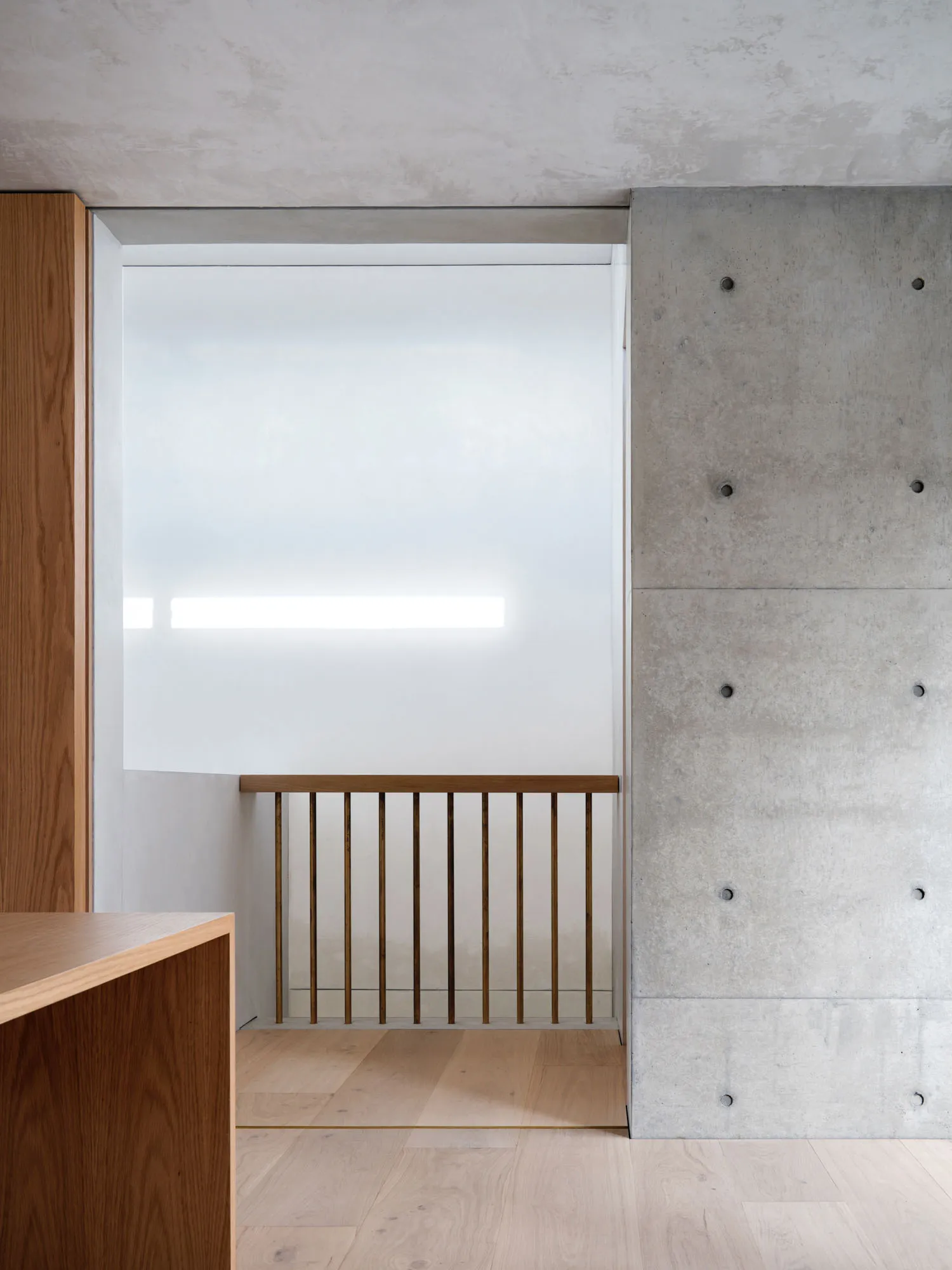 Contemporary interior design featuring a concrete wall, brass banister, and oak flooring.