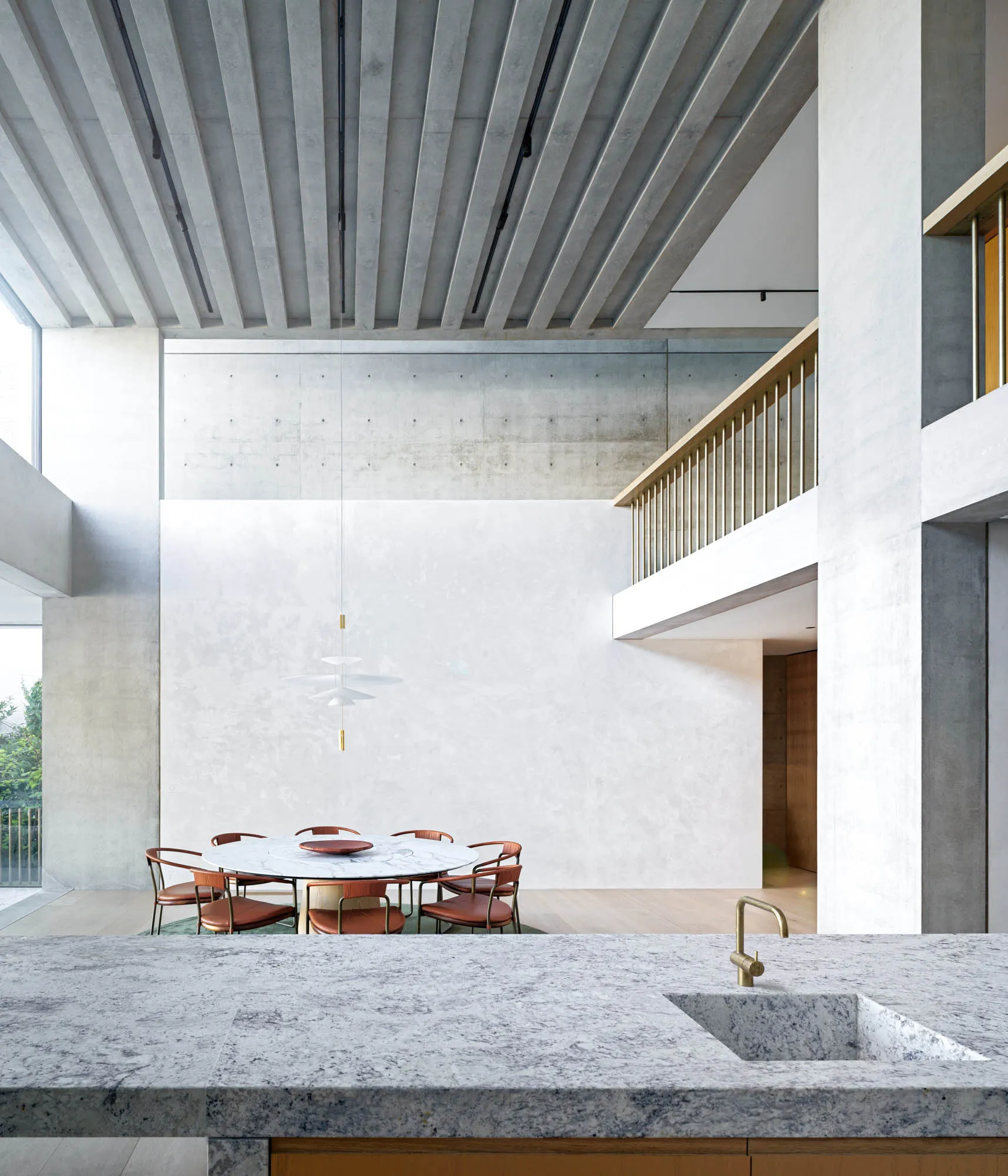 A modern dining room featuring a circular marble table surrounded by orange chairs, set against a concrete wall and illuminat