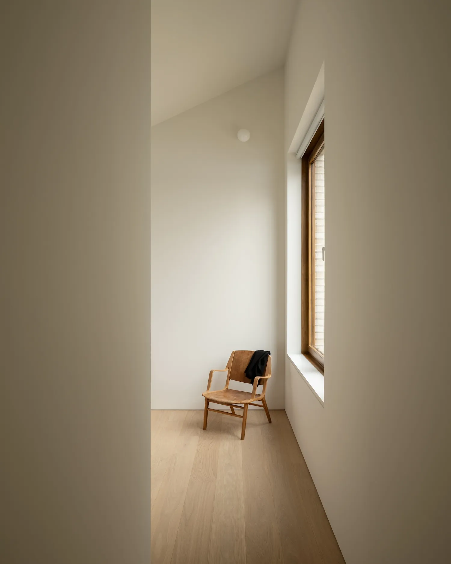 A minimalist bedroom with a wooden chair and a window.