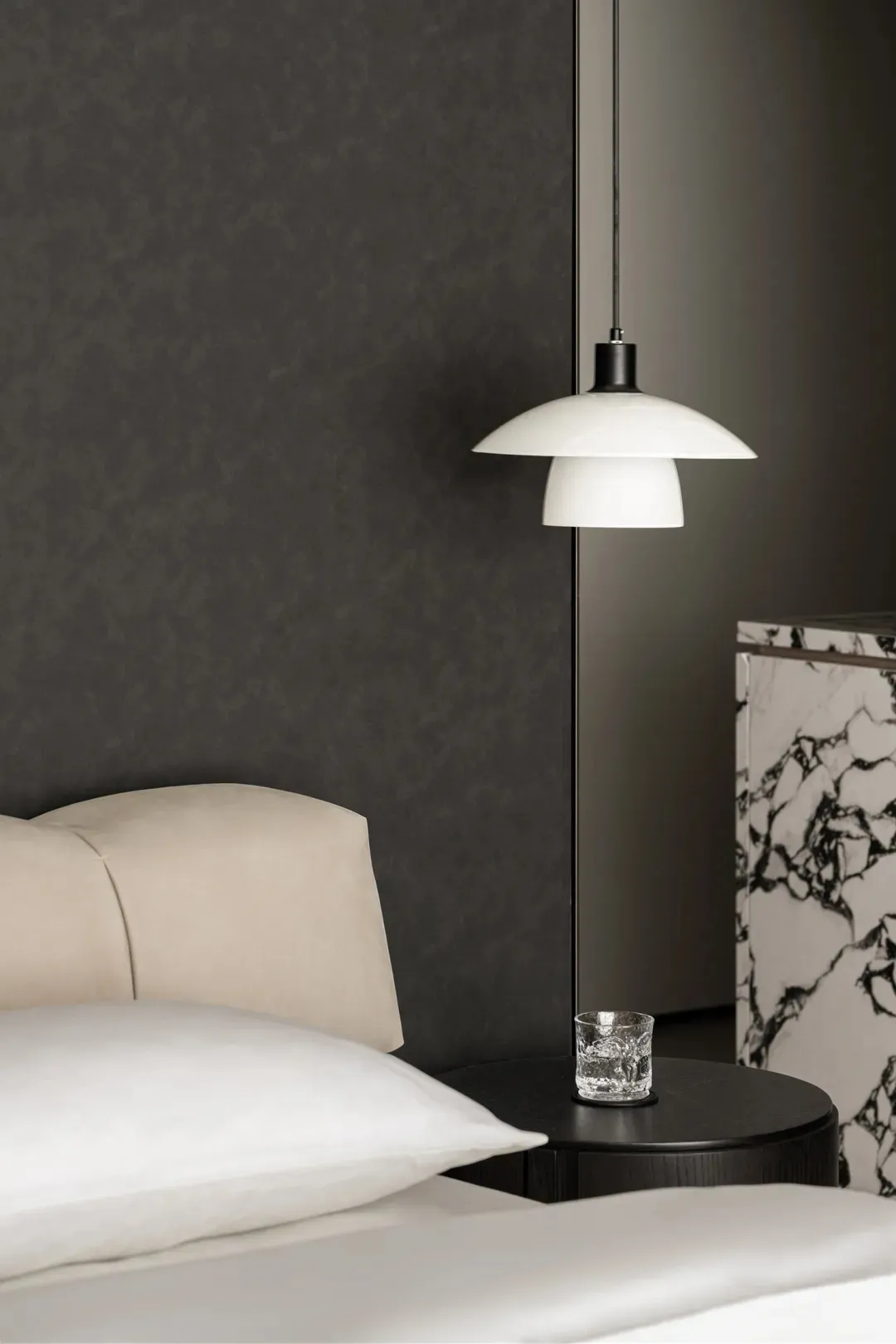 A minimalist bedroom featuring a marble bedside table and a white pendant lamp.