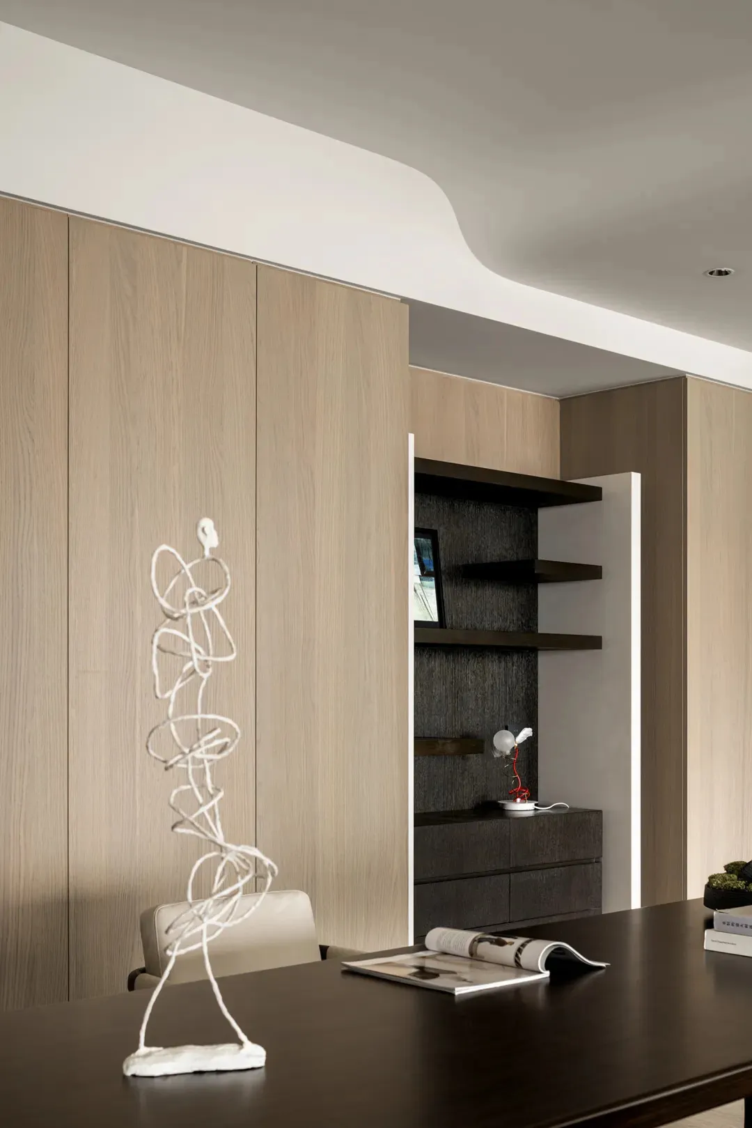 A modern minimalist office space featuring wooden shelves and a sleek desk with a sculpture and magazine on top.