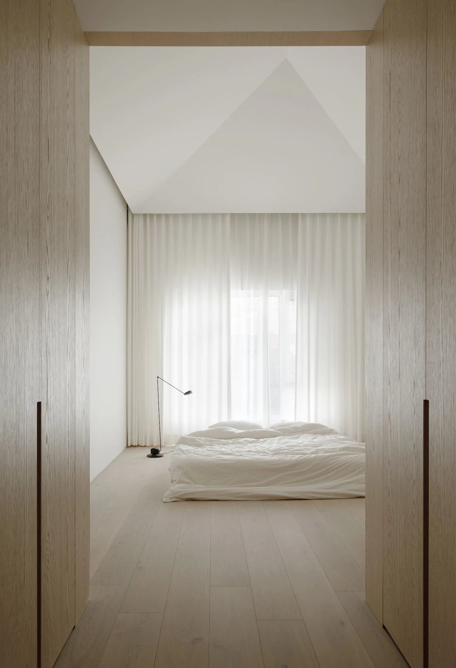 A minimalist bedroom with a bed, lamp, and sheer curtains.