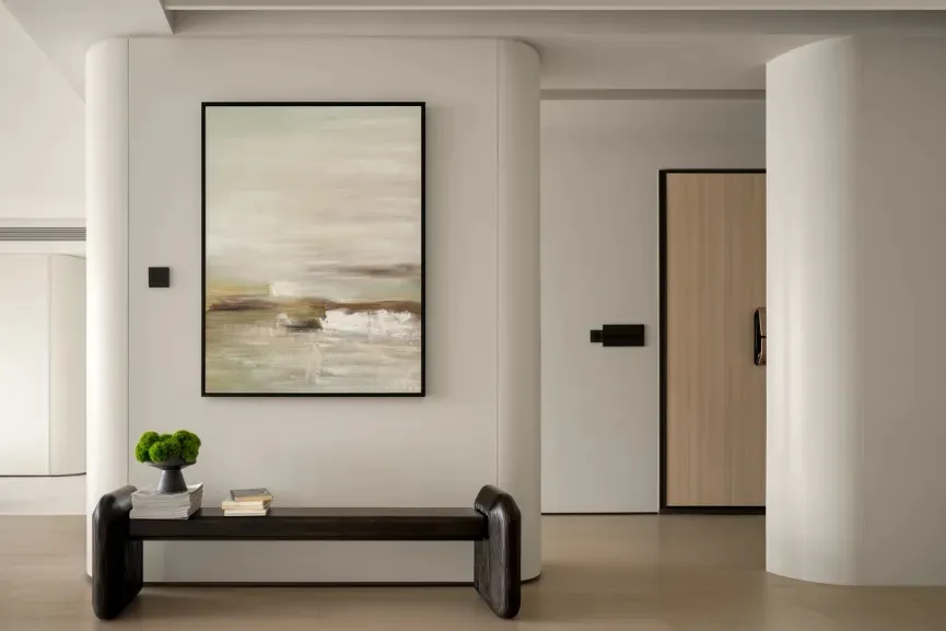 Modern white minimalist residential entryway with abstract painting and wooden bench.